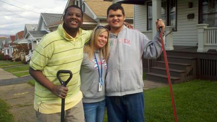 Two men and a woman smile with shovels in a neighborhood